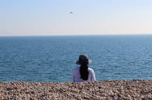image of a girl wearing a hat staring at the vast blue ocean