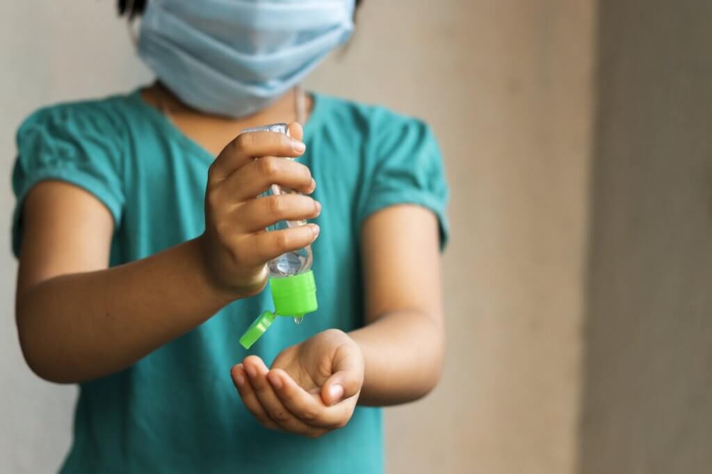a girl wearing face mask using hand sanitizer